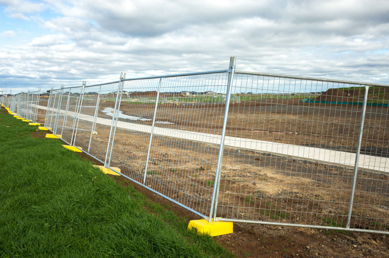 The Temporary Metal Barrier Fence On A Large Construction Site With Some Large Piles Of Dirt. Concept Of Real Estate Development, Infrastructure Construction And New Suburb. Melbourne, Vic Australia.